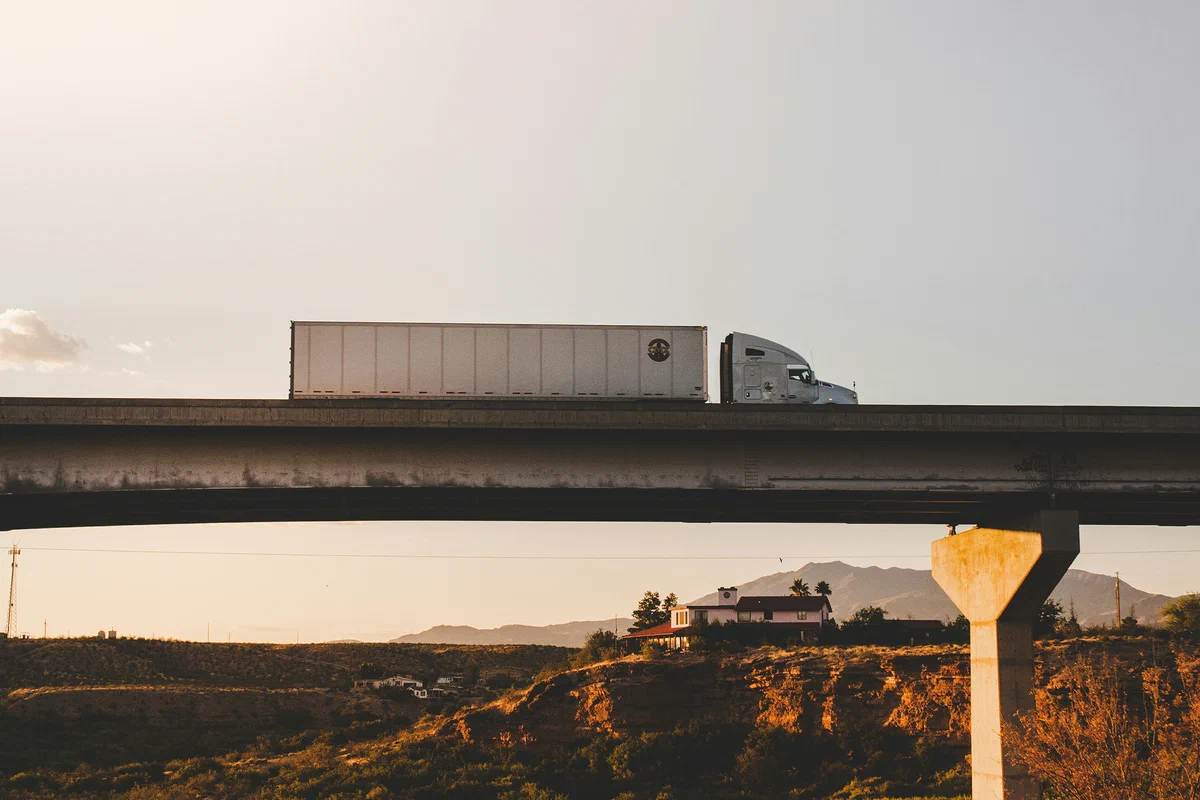 A photograph of a semi truck driving over a bridge.