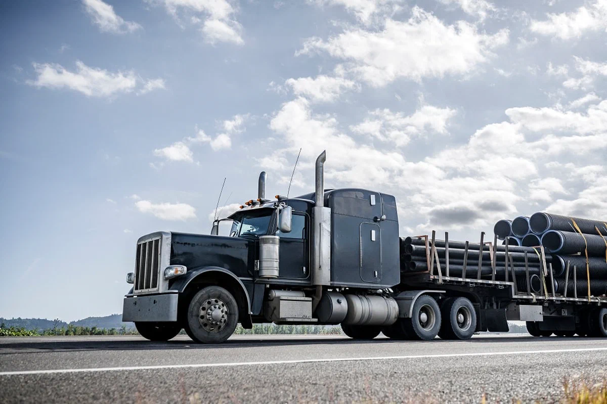 A photograph of a semi truck hauling large steel pipes. A photograph of a semi truck hauling large steel pipes.