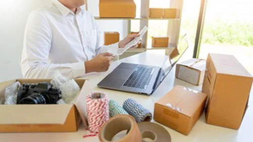 A man sitting at a desk with a laptop and boxes on the desk.
